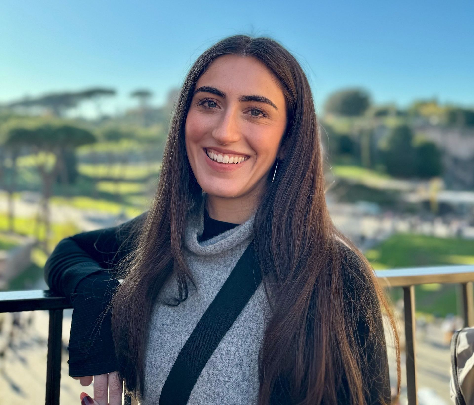 A woman with long hair is smiling while leaning on a railing.