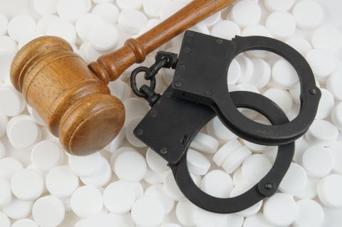 An image of a wooden law gavel and black handcuffs on top of prescription pills
