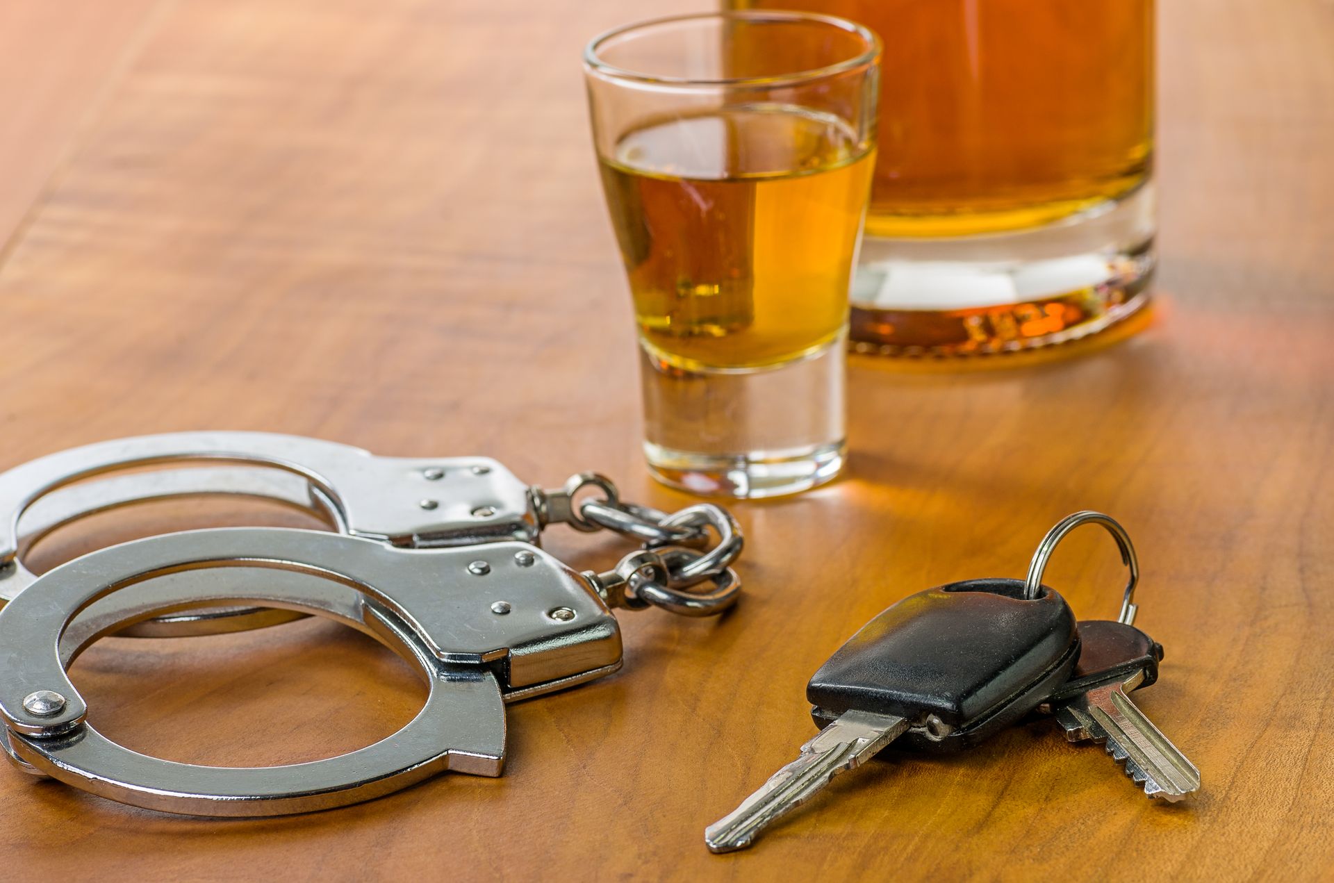 An image of handcuffs and car keys next to a small glass of whiskey and a large glass of whiskey