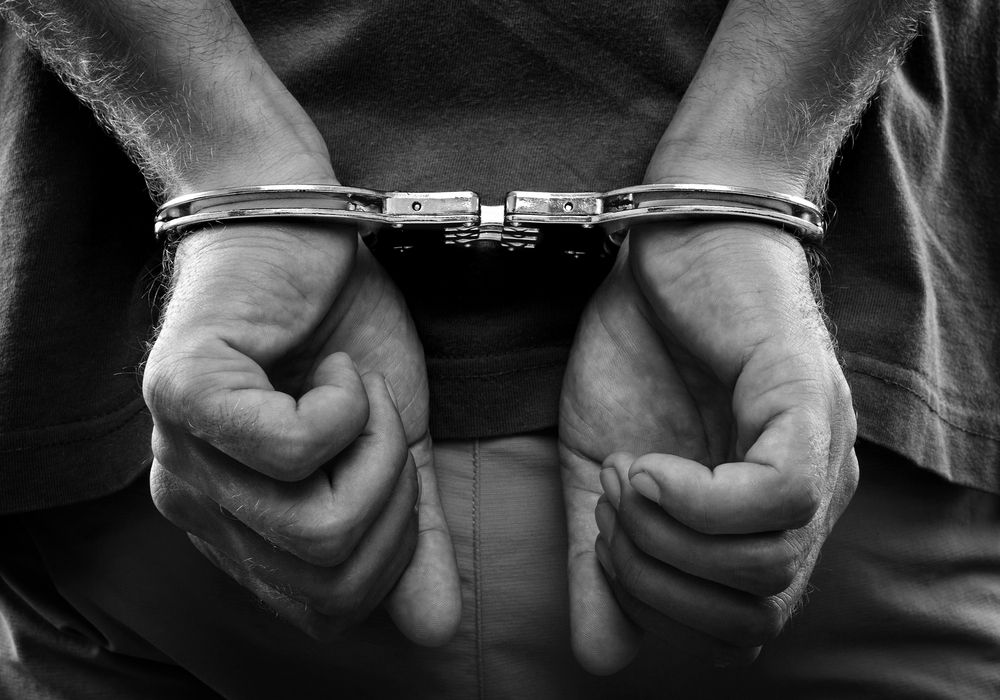 An image of a man's hands behind his back in handcuffs