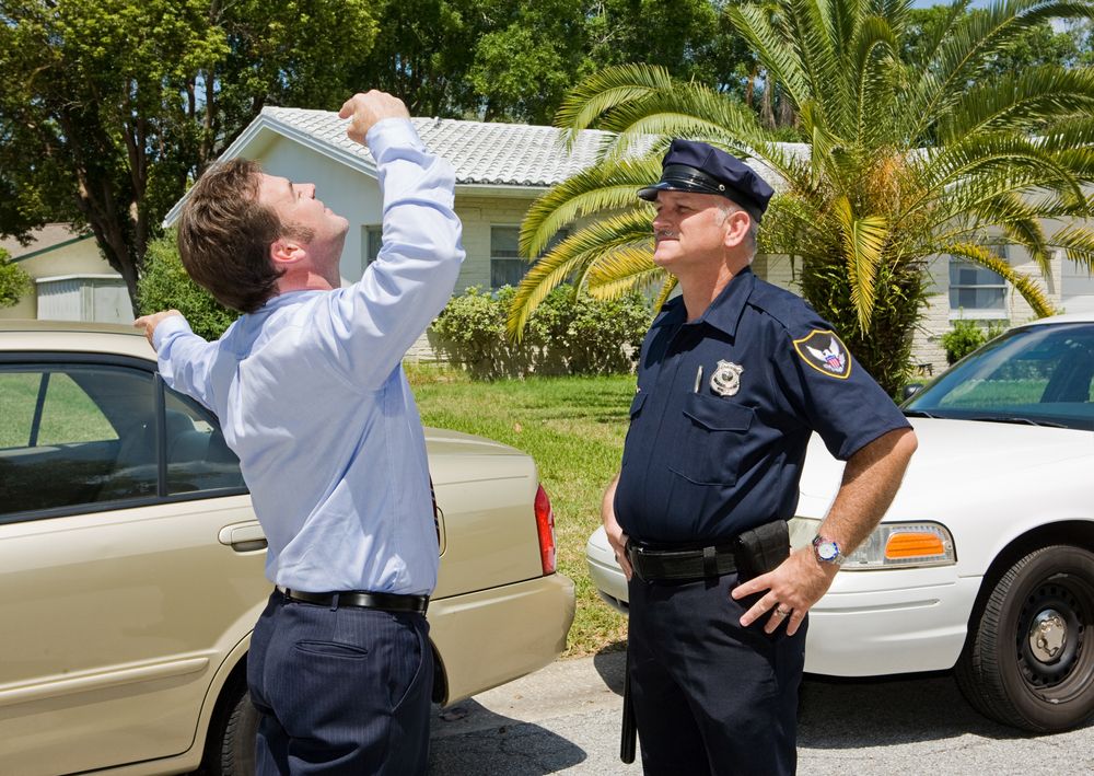 An Image of a man performing the finger to nose field sobriety test as a police officer watches