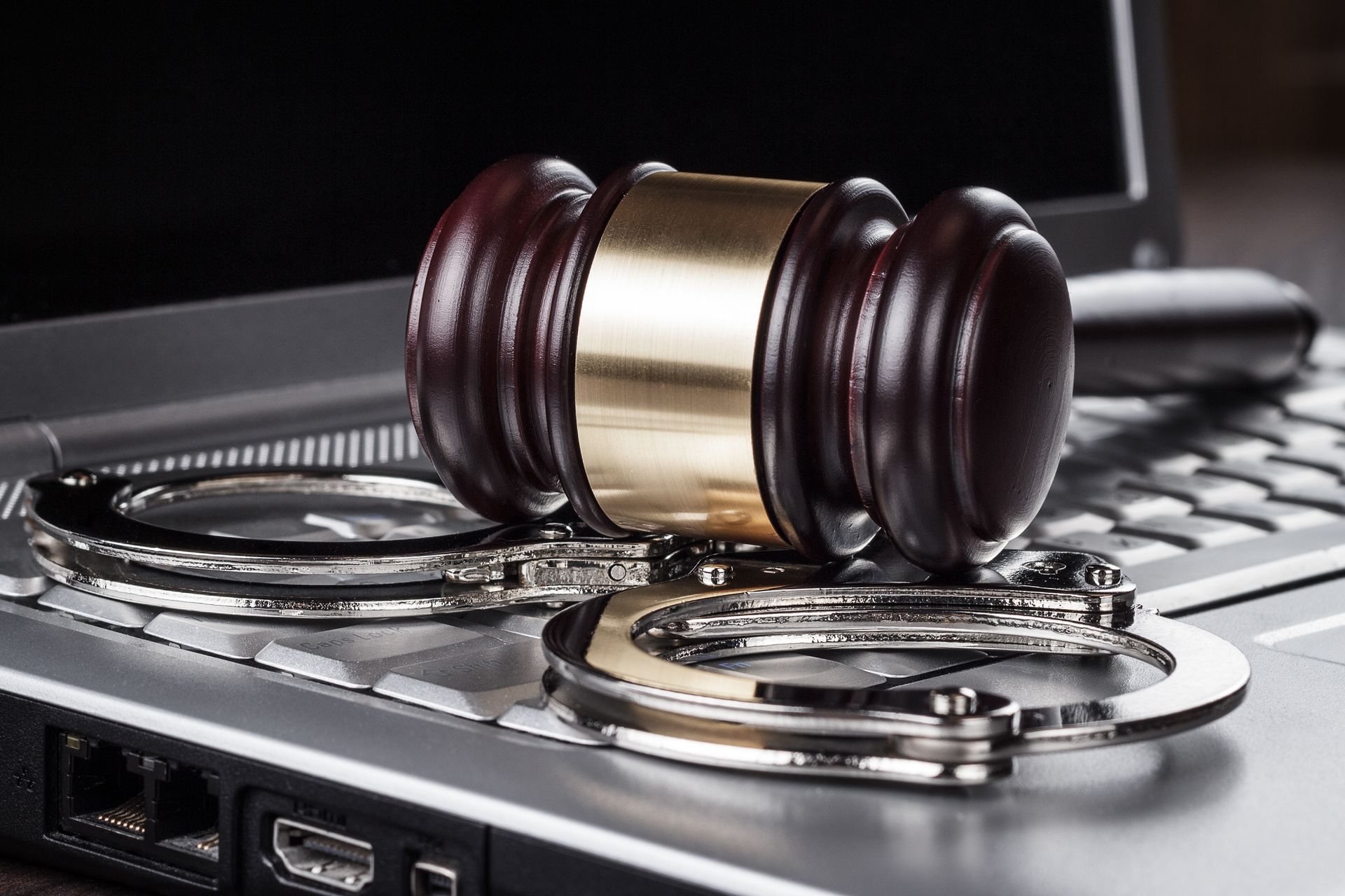 An Image of a laptop computer with a gavel and handcuffs lying on the keyboard