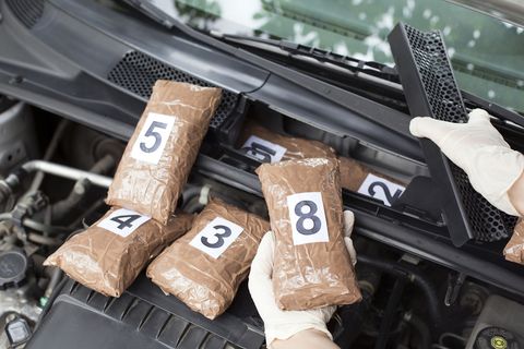 An image of numbered bags of drugs being removed from a car engine compartment