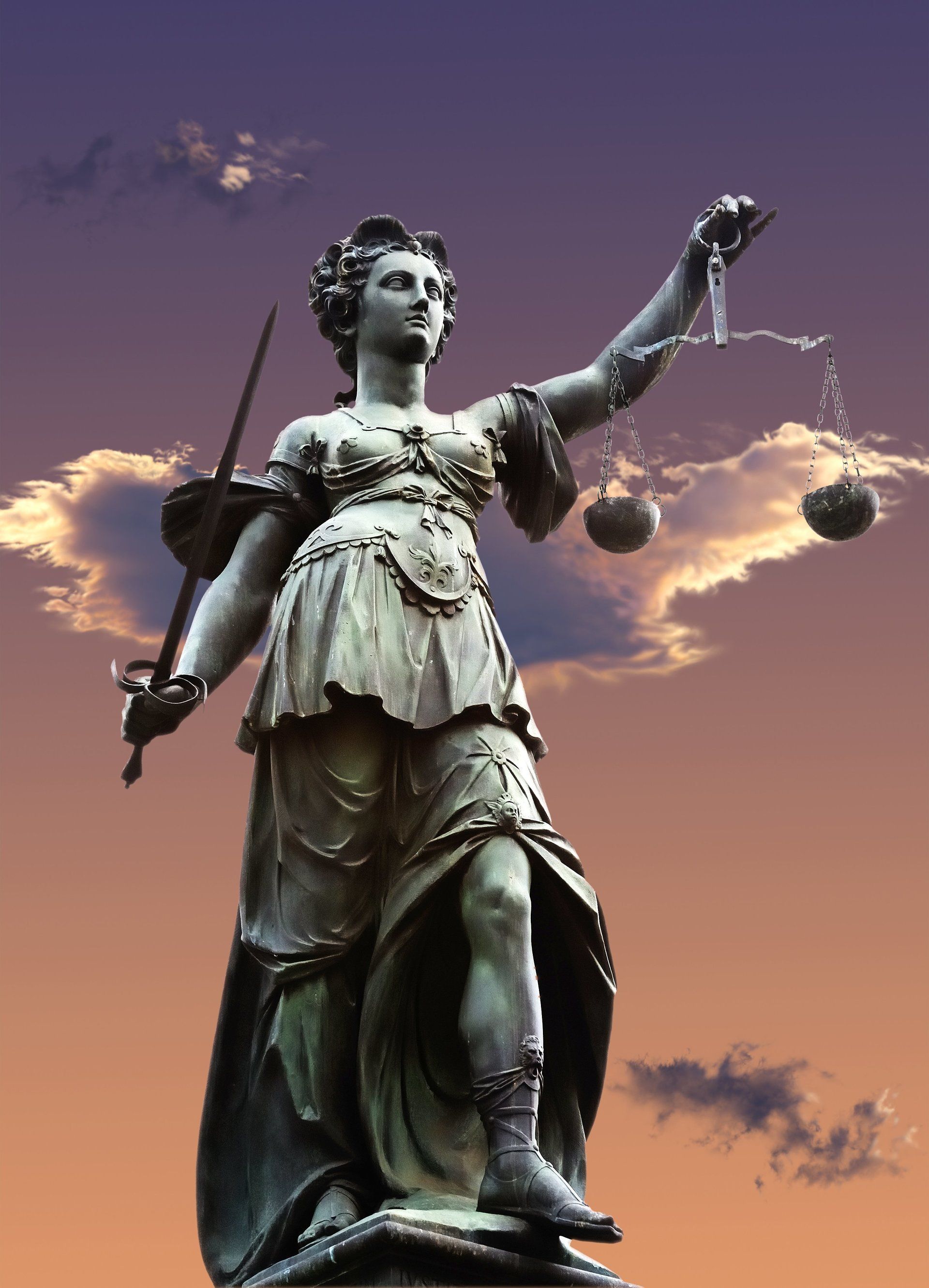 An image of a statue of Lady Justice with a sunset sky in background