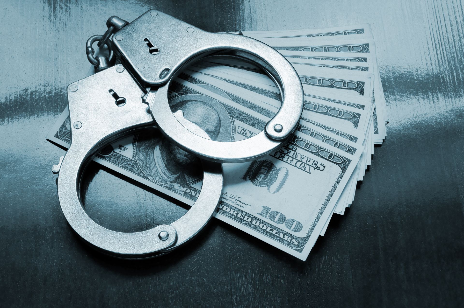 An Image of a set of handcuffs on top of fanned out one hundred dollar bills