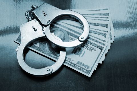 An image of a set of handcuffs on top of fanned out $100 bills