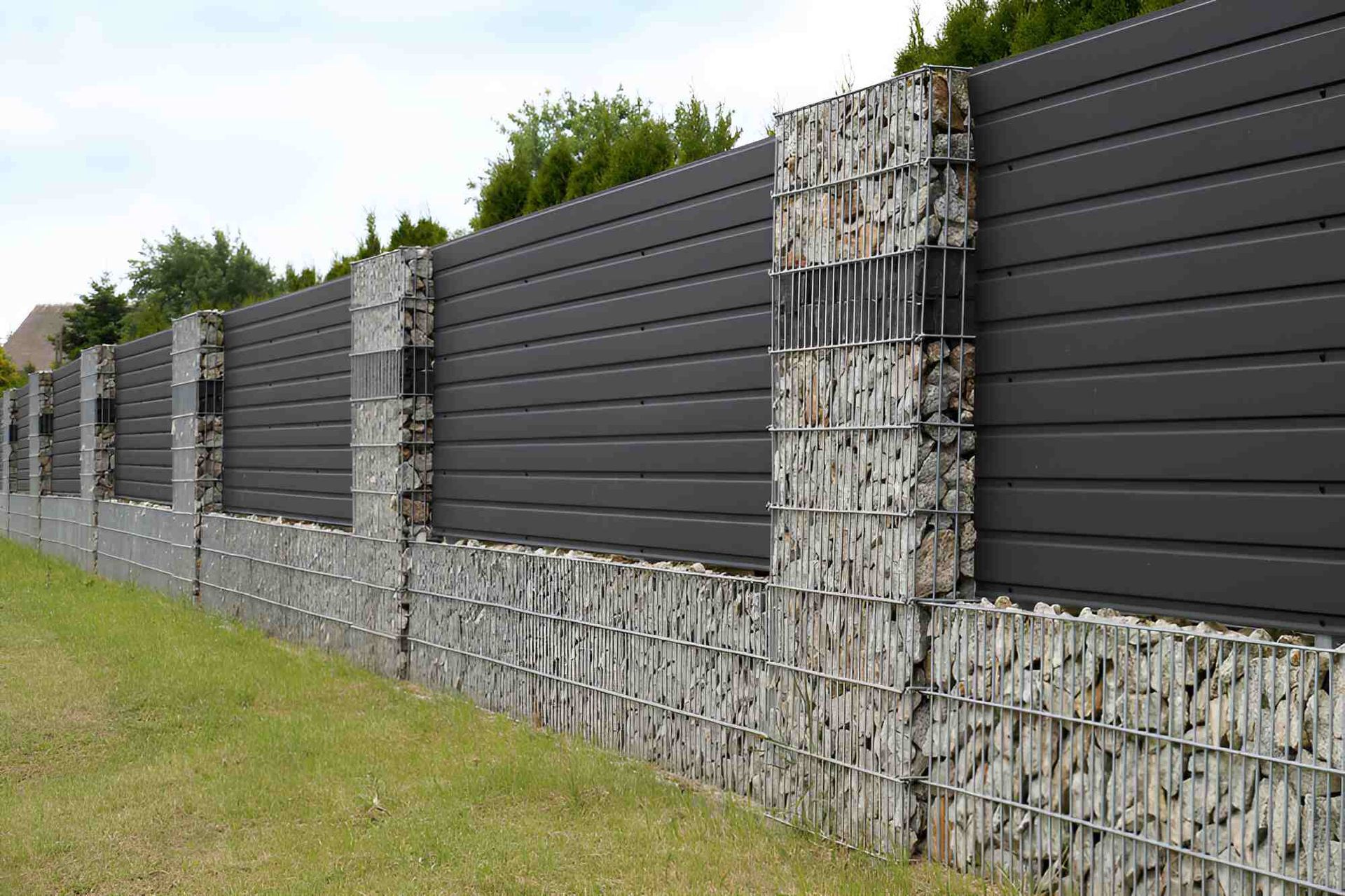 A Black Fence With A Lot Of Rocks Behind It — Affordable Underpinning Solutions In Kiama, NSW
