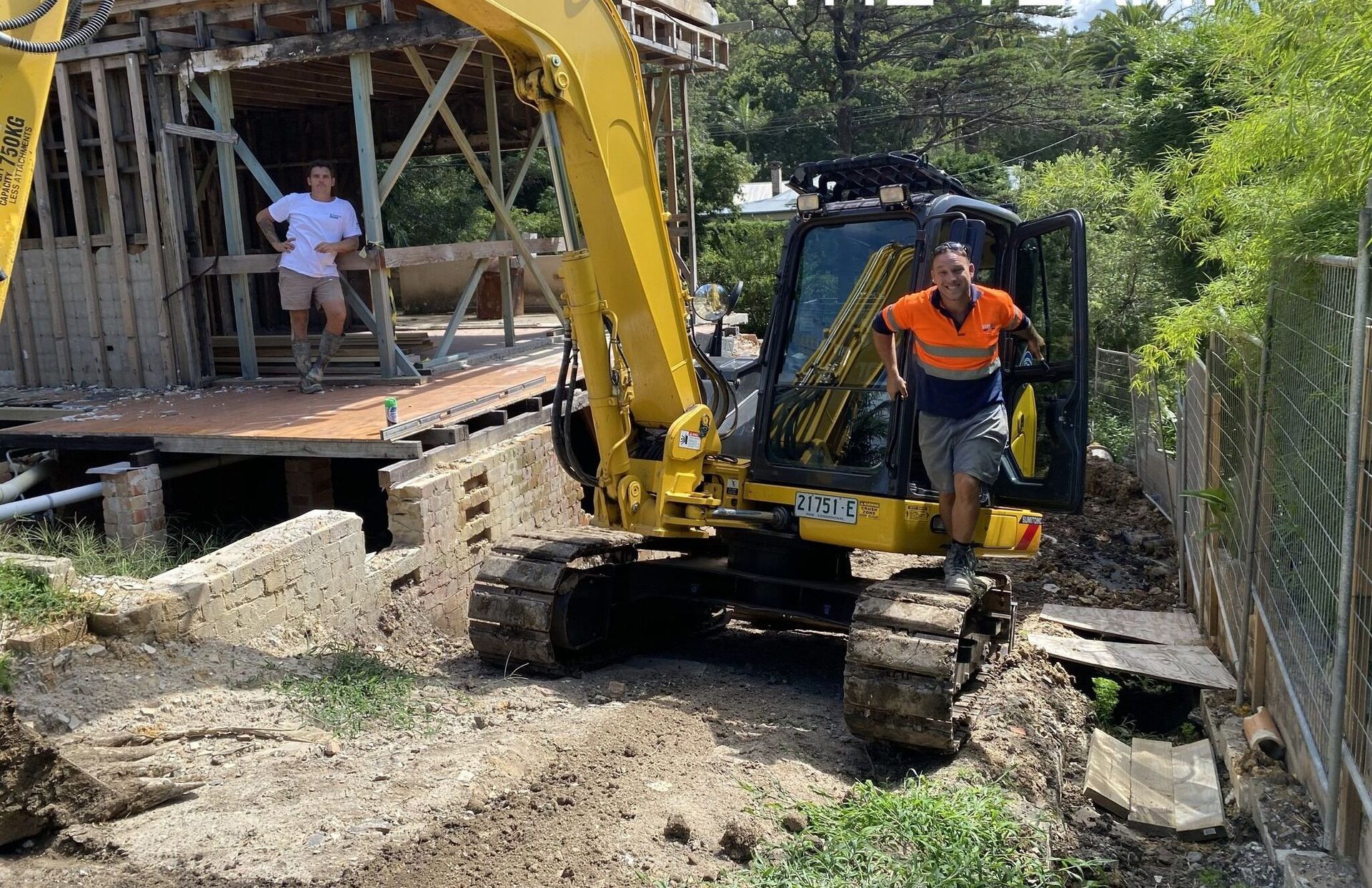 A Man Is Standing In Front Of A Yellow Excavator — Affordable Underpinning Solutions In Shell Cove, NSW