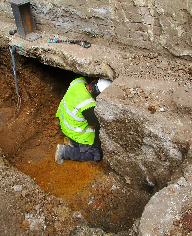 A Worker in High Vis Vest Underpinning a Building — Affordable Underpinning Solutions In Newtown, NSW