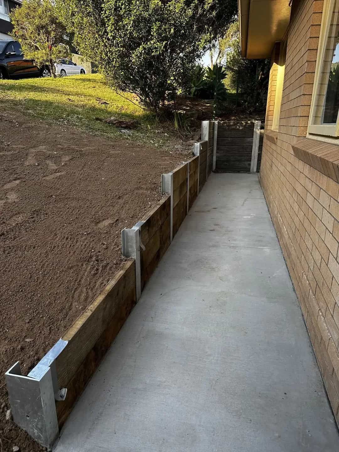 A concrete walkway with a wooden retaining wall — Affordable Underpinning Solutions In Shell Cove, NSW