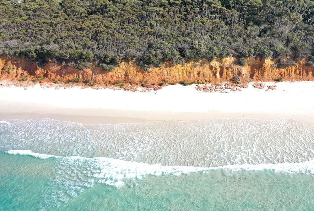 An Aerial View Of A Beach Surrounded By Trees And A Body Of Water — Affordable Underpinning Solutions In Jervis Bay, NSW