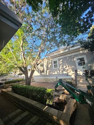 A house exterior with a tree, a brick retaining wall, and a small excavator.