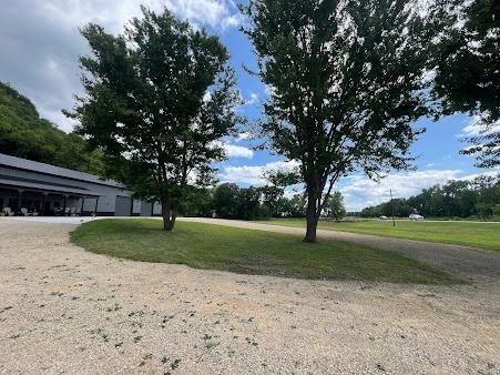 Gravel driveway leading to a building with trees, grass, and a blue sky with clouds.