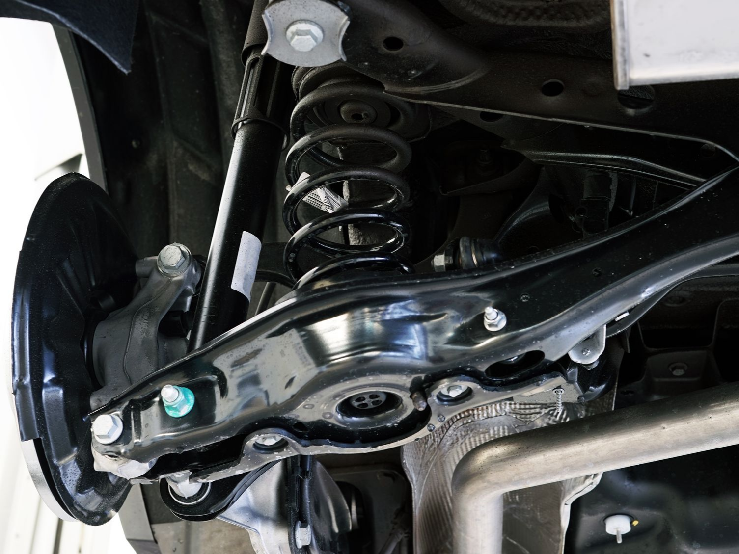 Close-up of a car’s rear suspension with coil spring, control arm, and brake assembly.