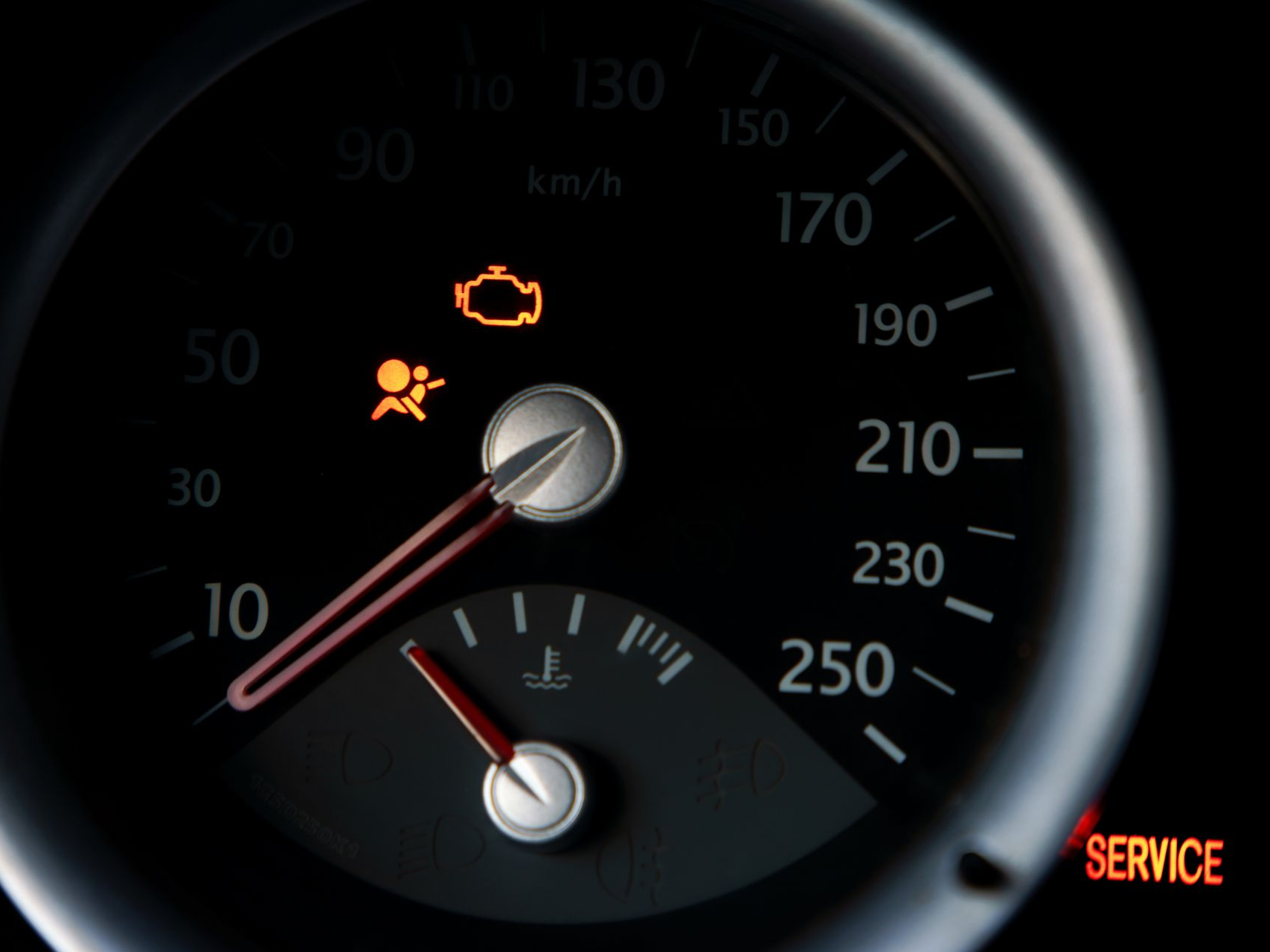 Car dashboard gauge cluster with warning lights and a service indicator illuminated