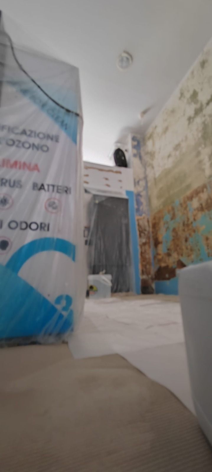 Stretto corridoio con pareti a vista, uno striscione blu e bianco sulla sinistra e una porta in fondo.