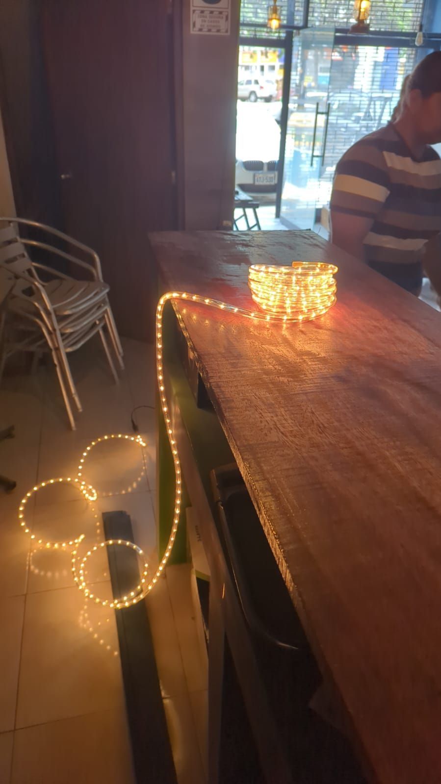 Tavolo di ristorante in penombra con lucine decorative e una persona seduta sullo sfondo.