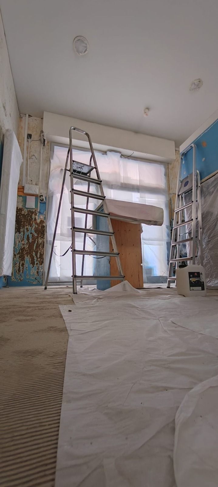 Scala in una stanza in fase di ristrutturazione, con pavimento coperto e finestre, luce proveniente dal retro.