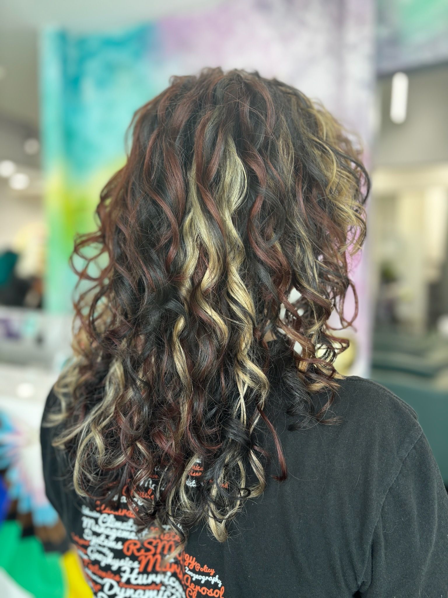Person with curly hair, highlighted blonde and red, in a salon setting.