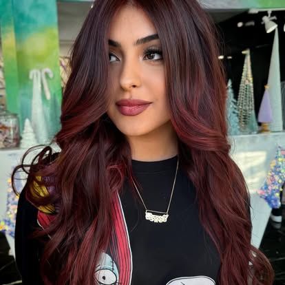 A woman with long red hair is wearing a black shirt and a necklace.