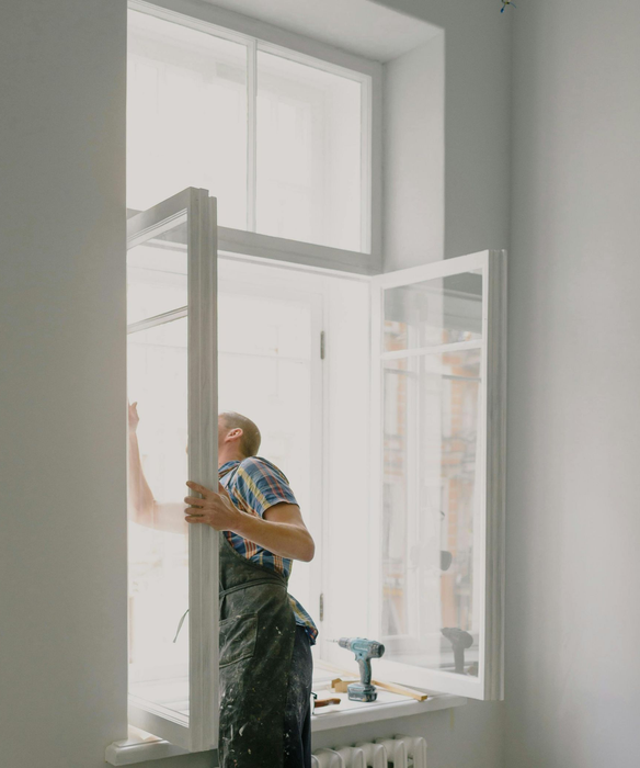 Worker installing a large window in a bright room with white walls and a high ceiling