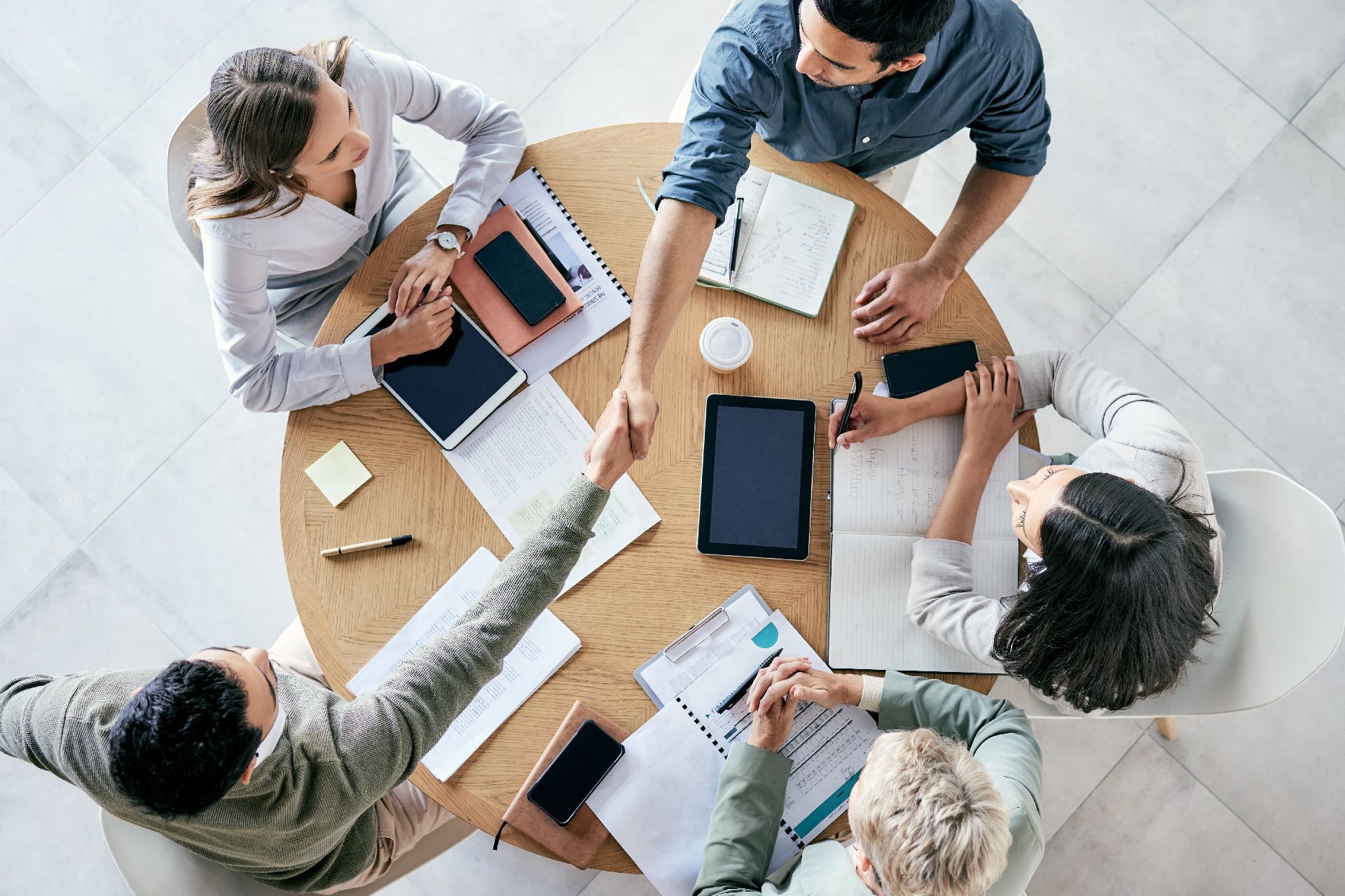 Equipo de negocios sentado alrededor de una mesa, apretándose las manos y colaborando en documentos.