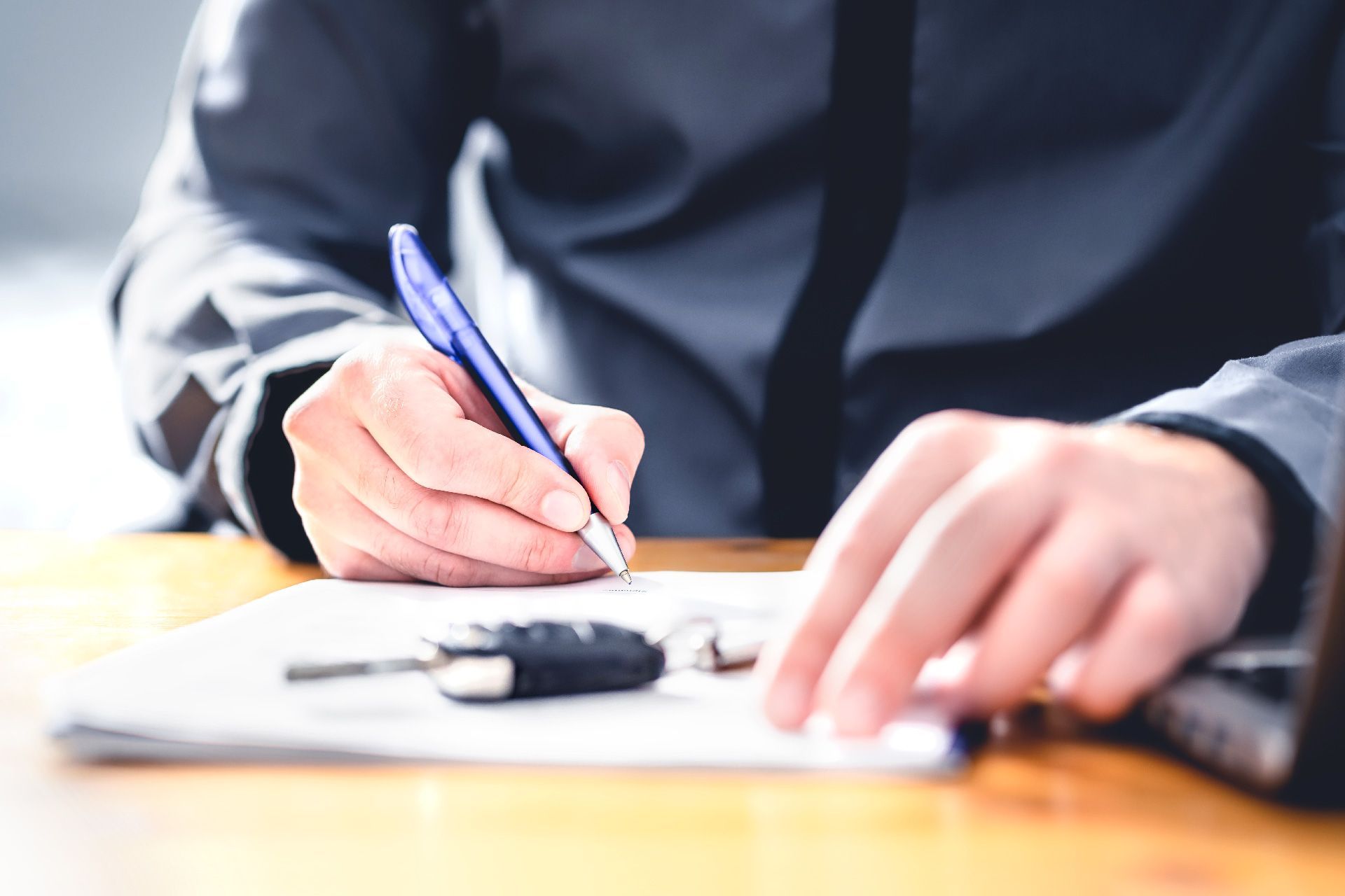 Persona firmando documentos de préstamo de automóvil, llave del automóvil en el escritorio.