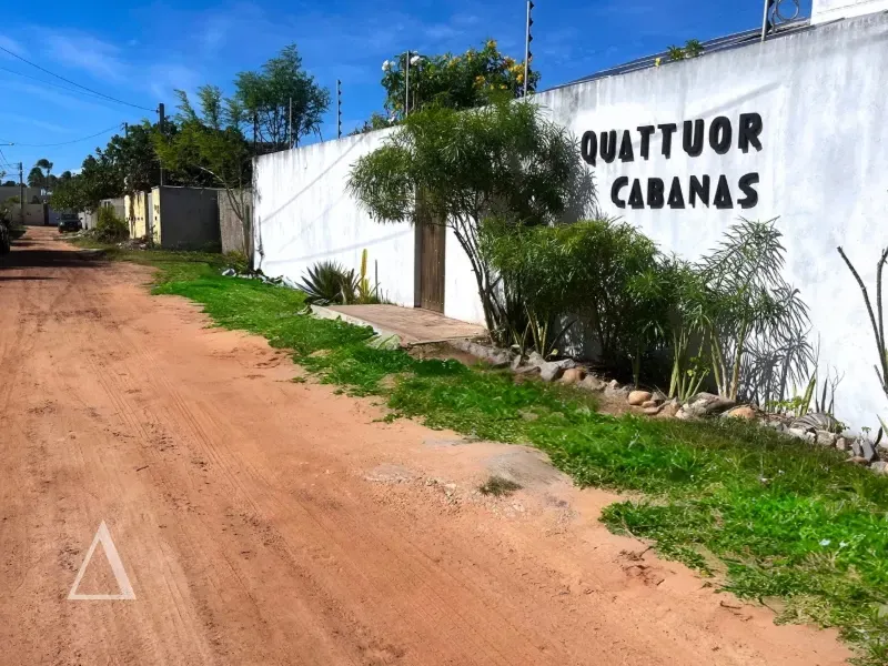 Fachada externa da Quattuor Cabanas com muro branco, letreiro identificando a pousada e vegetação local em São Miguel do Gostoso, Rio Grande do Norte.