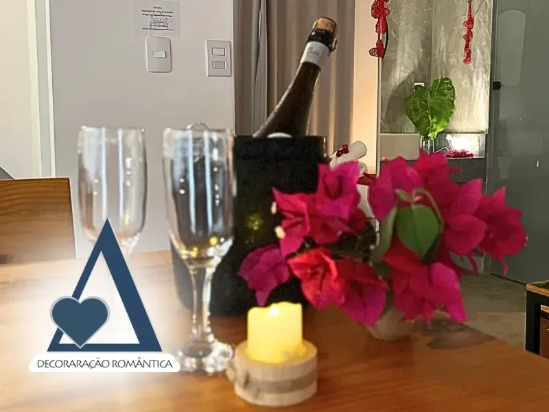 Detalhe de mesa posta com garrafa de espumante em balde, duas taças, vela acesa e flores, sob o selo de decoração romântica da Quattuor Cabanas em São Miguel do Gostoso.