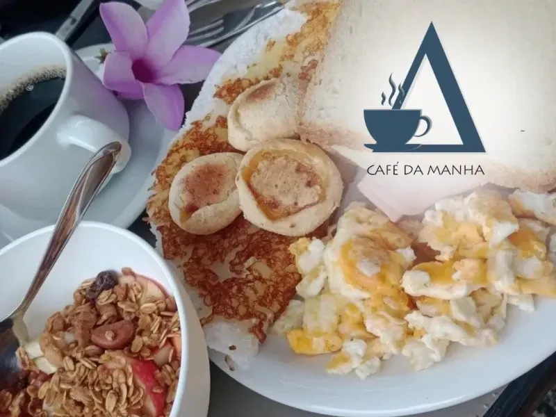 Close de um prato de café da manhã com ovos mexidos, tapioca, pães, uma tigela de granola com frutas e café, servido na Quattuor Cabanas em São Miguel do Gostoso.