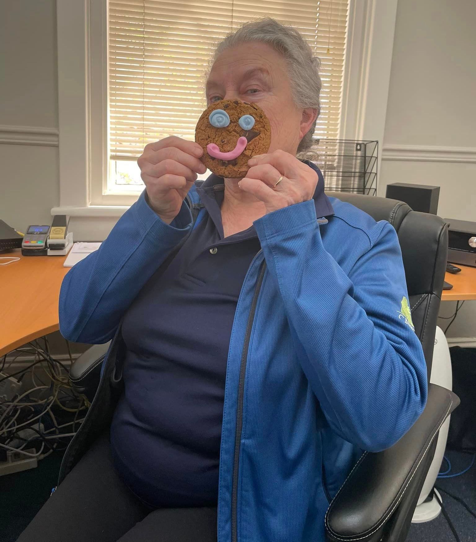 Une femme portant une veste bleue est assise sur une chaise et mange un bonhomme en pain d'épice.