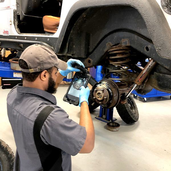 a man is working on a jeep with a tablet performing a digital vehicle inspection