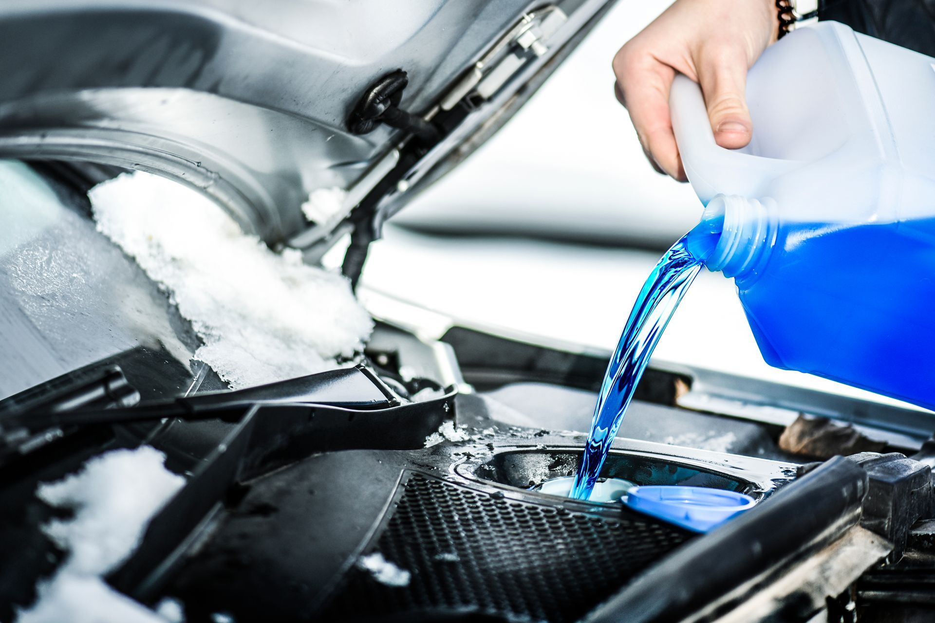 a person is pouring windshield washer fluid into a car .