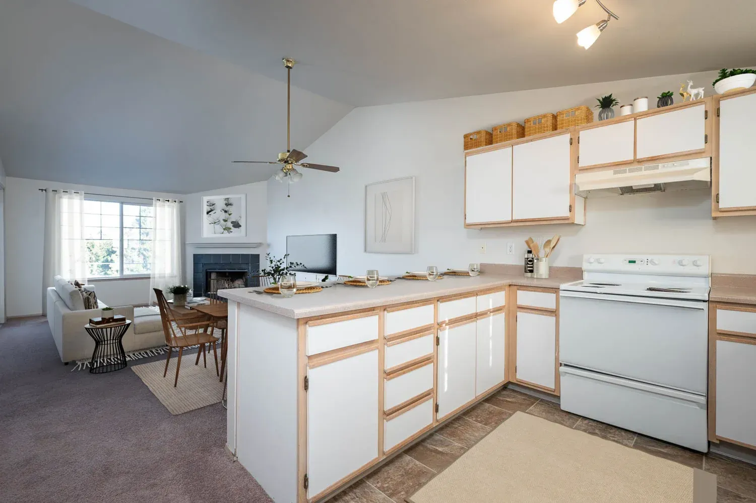 Open-concept living space with a kitchen, dining area, and living room. White cabinets, tan countertops, and a fireplace.