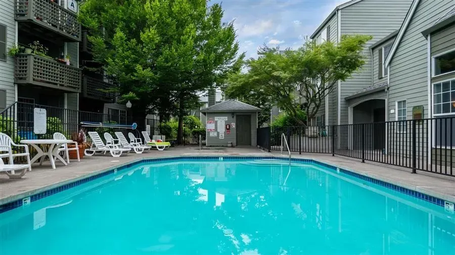 Swimming pool in front of apartment building, with lounge chairs and trees around it.