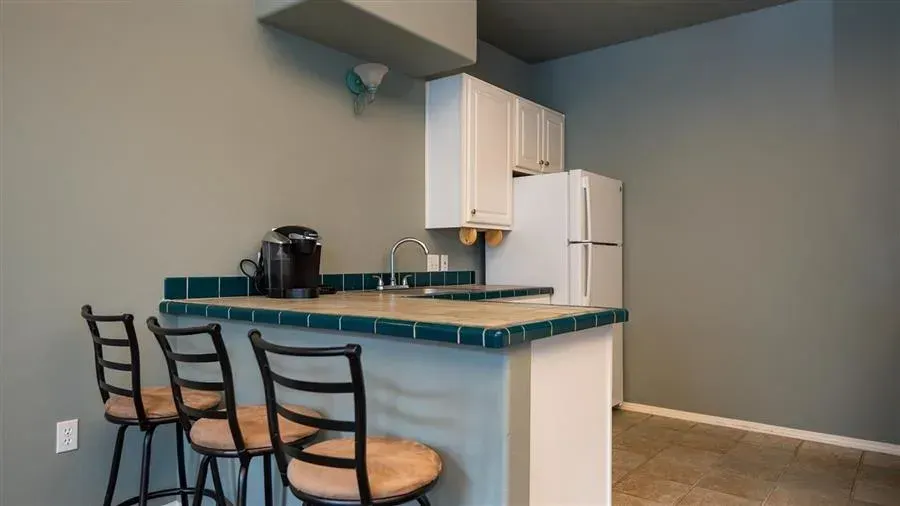 Small kitchen with a breakfast bar, white cabinets, and a refrigerator. Three bar stools and grey walls.