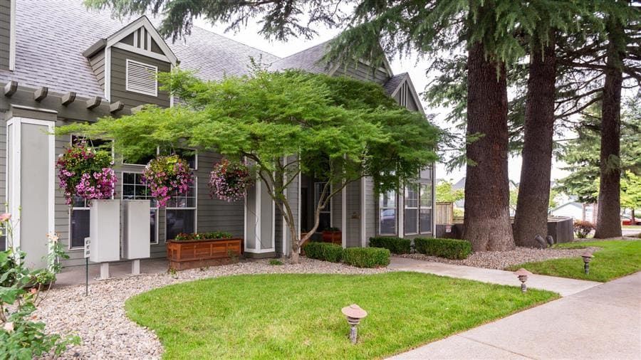 Green-sided building with gray roof and trim, landscaped lawn, and trees.