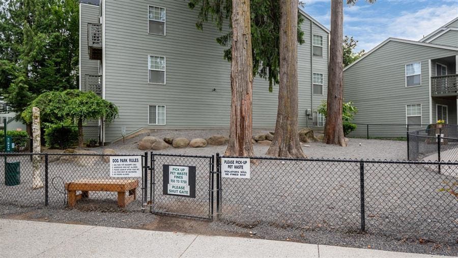 Dog park with fence, benches, and signs near a gray apartment building.