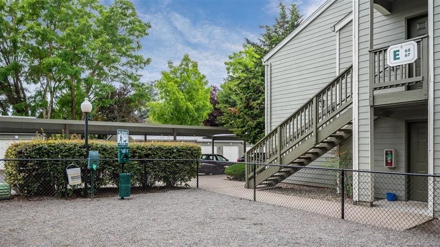 Apartment building exterior with staircase, gravel area, dog waste station, and carport.