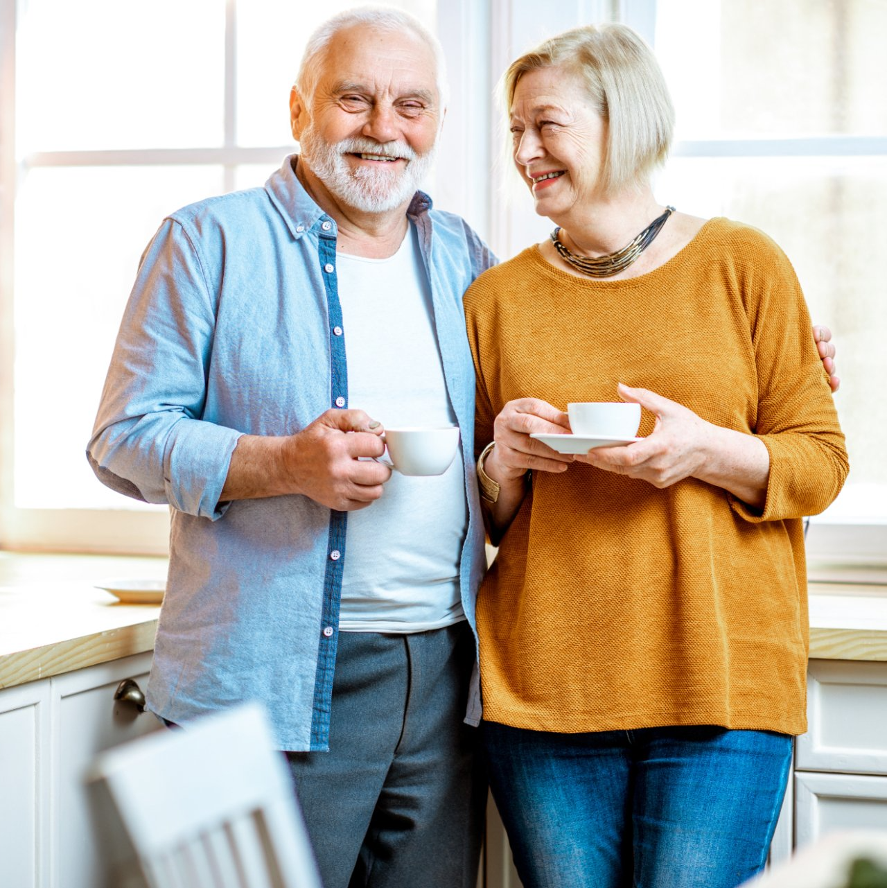 elderly caucasian couple posing holding coffee cups in kitchen