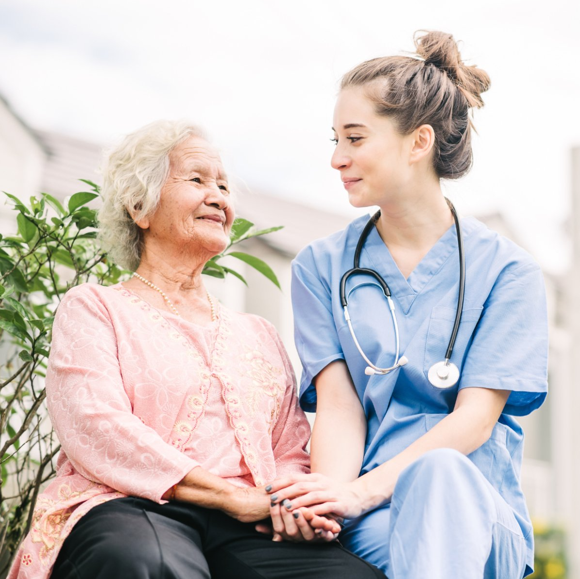 elderly asian woman sitting with young senior center nurse outside