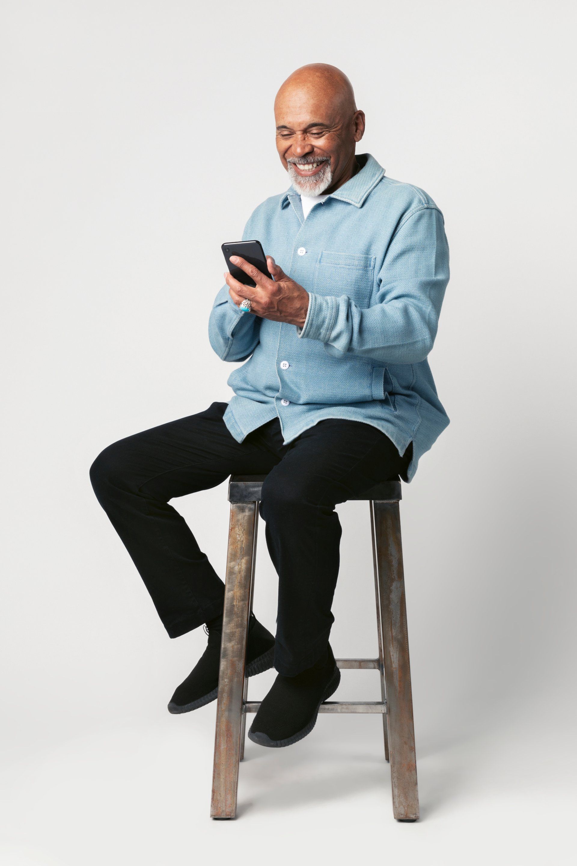 senior black man sitting on stool using smartphone