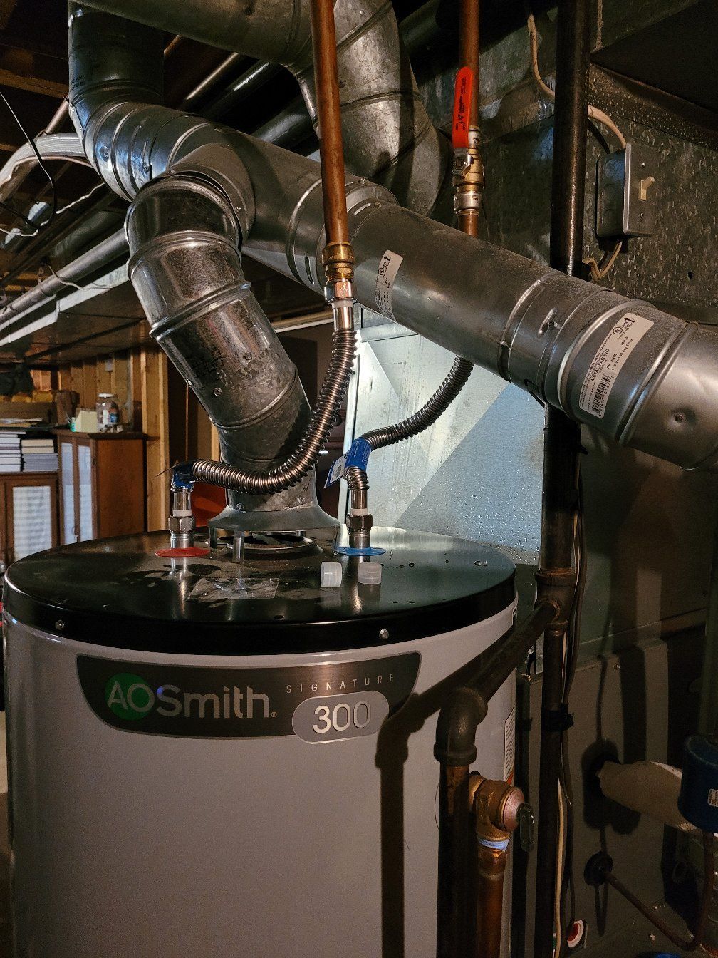 A water heater is sitting in a basement next to pipes.