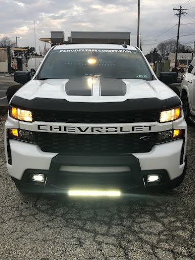 White Chevrolet Silverado truck with black accents, light bar, and hood stripes.