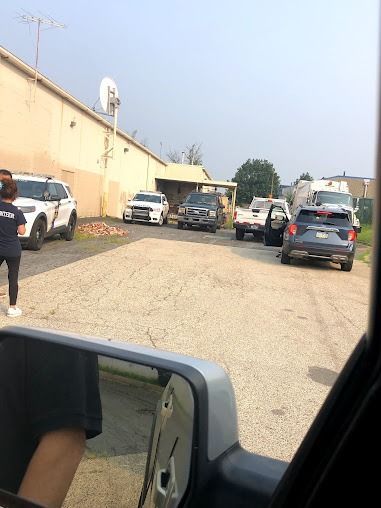 Several police vehicles are parked on a gravel lot near a beige building.