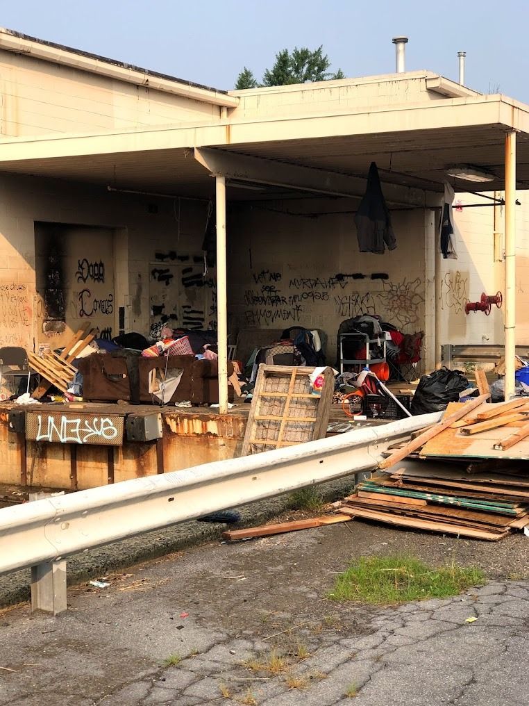 Exterior of a building with graffiti and a cluttered loading area. Debris includes wood, bags, and pallets.