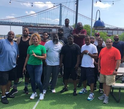 Group of people posing outdoors near a bridge. Some are smiling, in casual attire, on artificial grass.