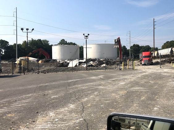 Demolition site with two large white tanks being dismantled by excavators, truck nearby.