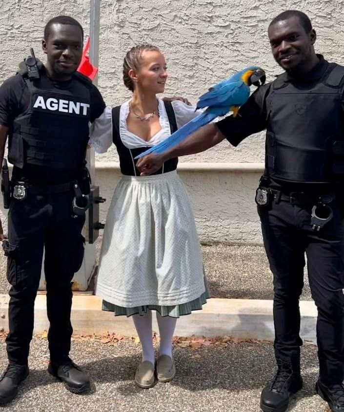 Two security guards flank a woman in traditional dress, holding a blue-and-yellow macaw.