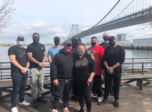 Group of people wearing masks posing by a bridge over water. Some wearing casual clothes.